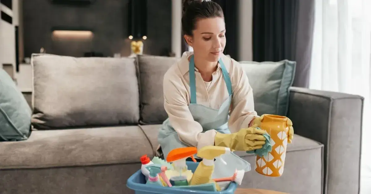 Woman wiping home decor with cleaning supplies while following practical house cleaning tips.
