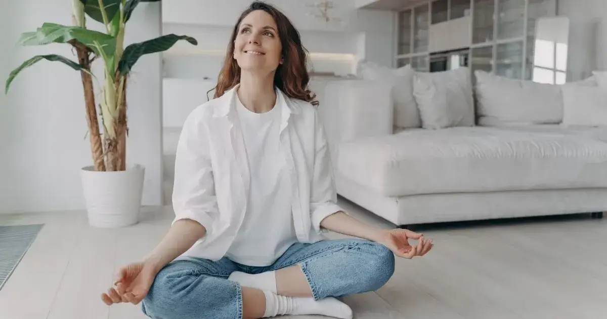 Woman meditating in a bright living room, showing the connection between clean spaces and mental health.